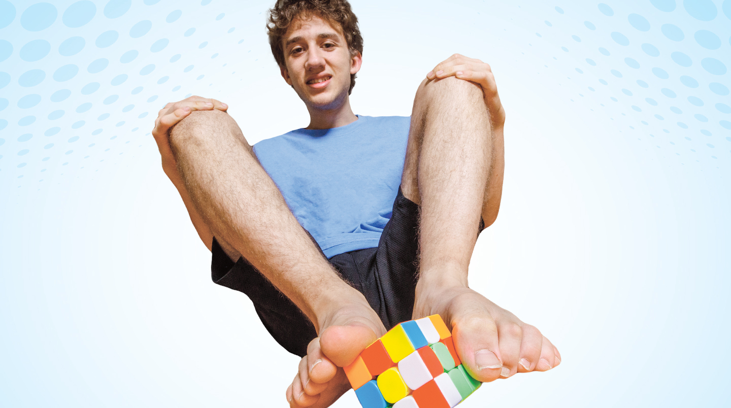 A young man solves a Rubik’s cube with his feet.