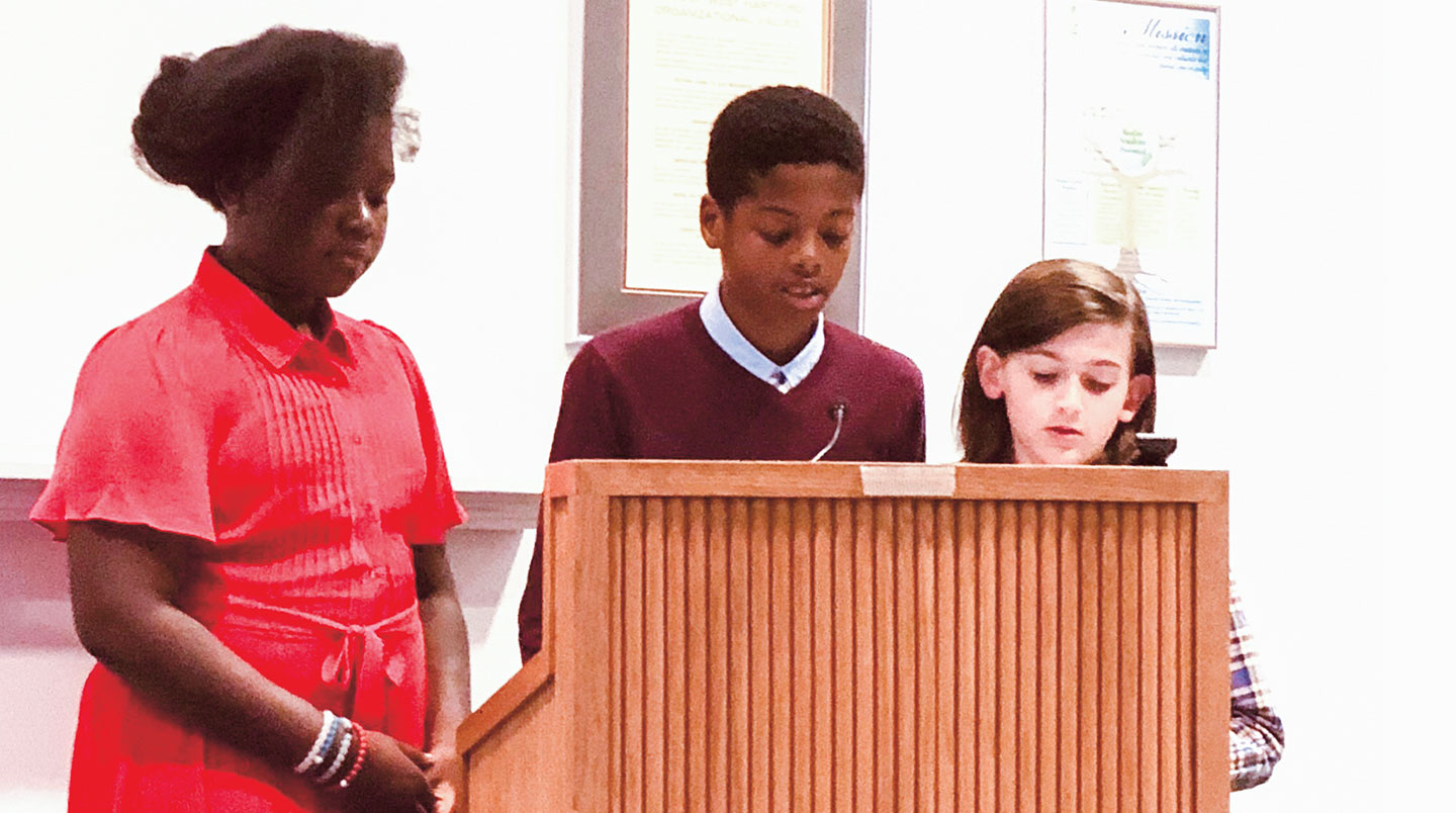 Three kids speak at a podium