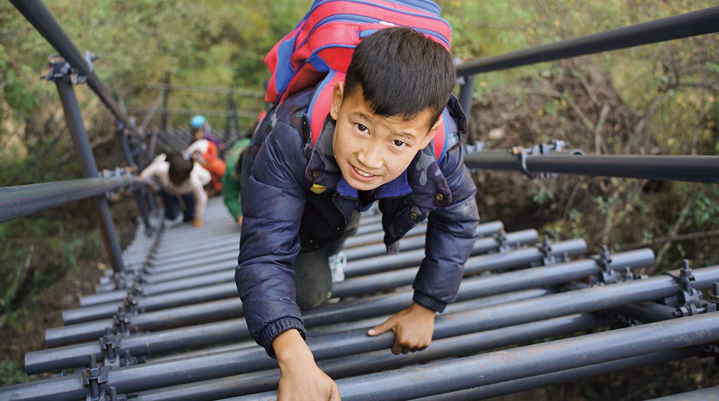 A school kid climbs a metal ladder on the side of a cliff.