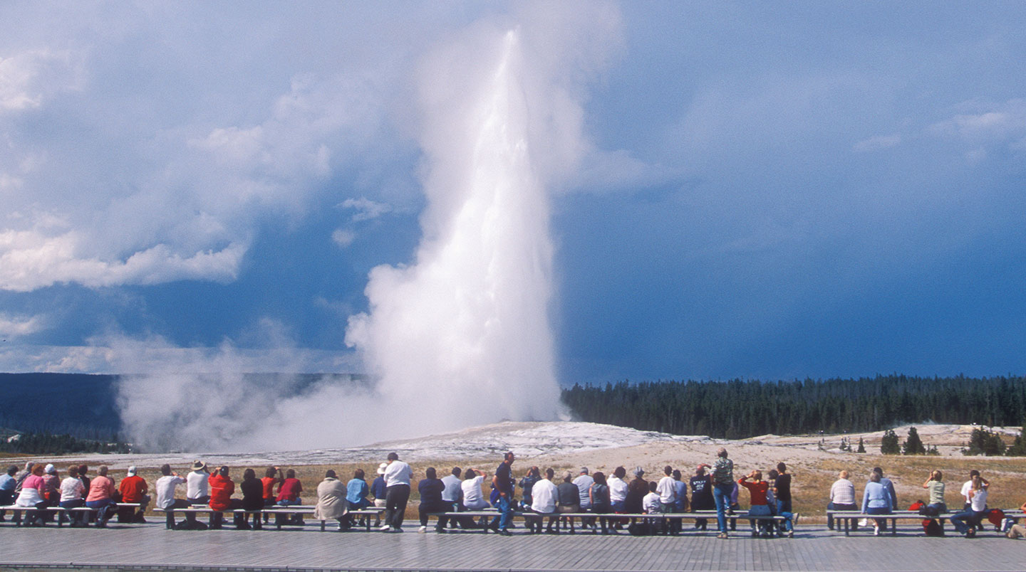 Old faithful erupts as visitors watch.