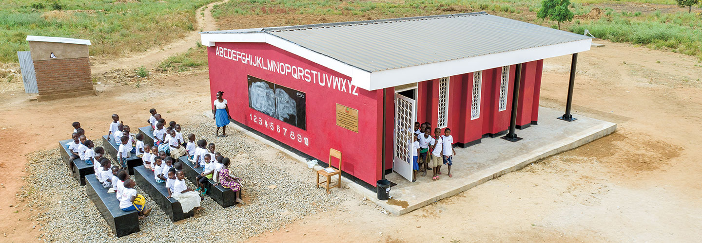 Students and teacher in front of their red 3-D printed school