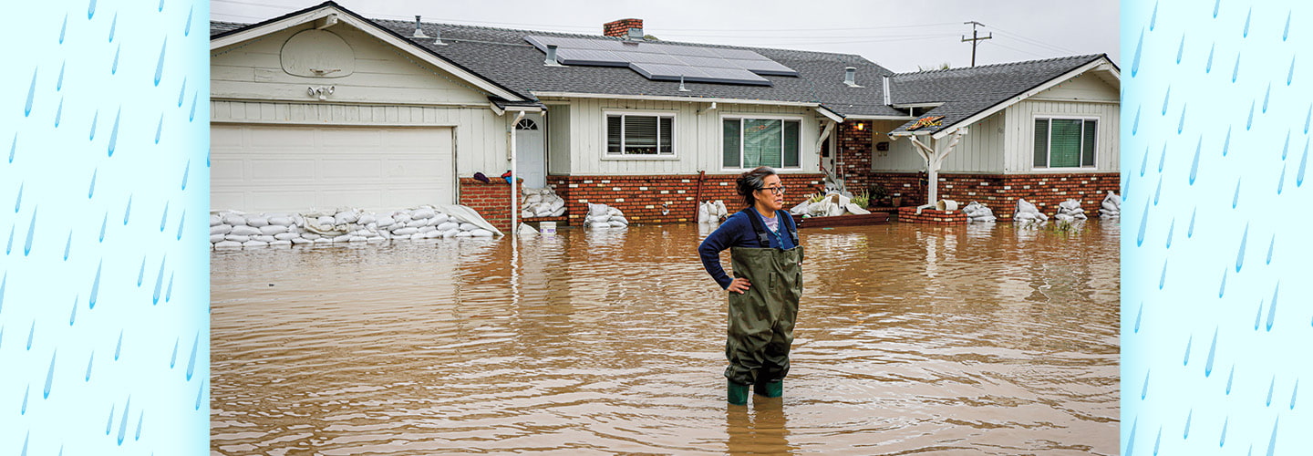 Photo of a person standing in a flooded street in front of a home halfway underwater