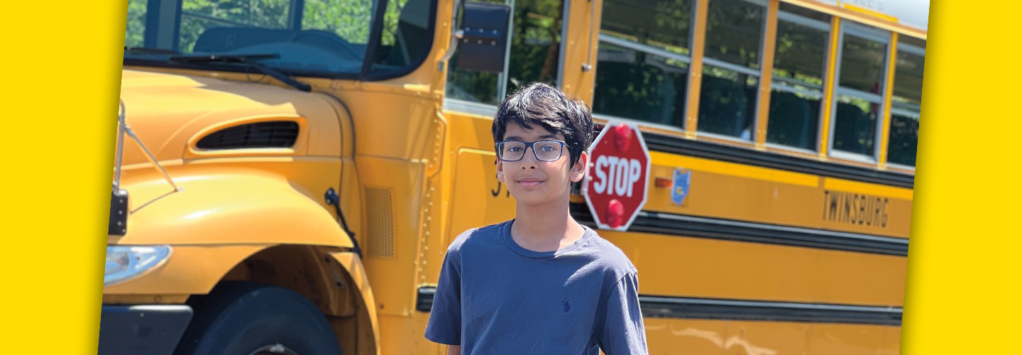 Photo of a person posing with a schoolbus in the background