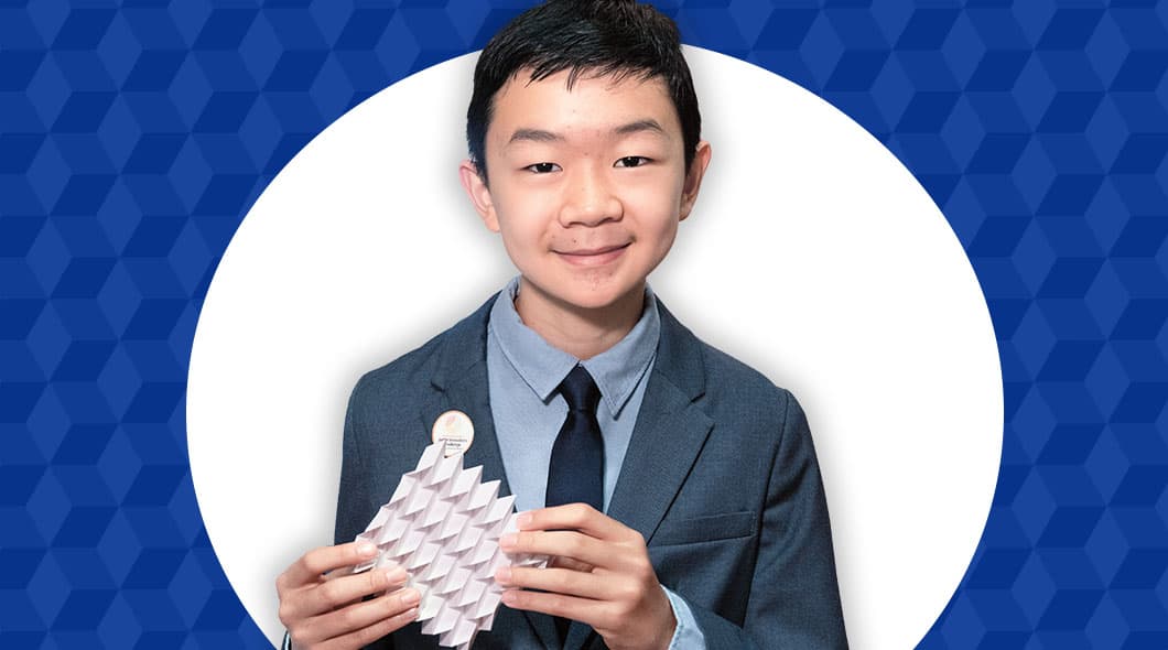 A boy in a gray suit and tie holds a white geometric paper sculpture