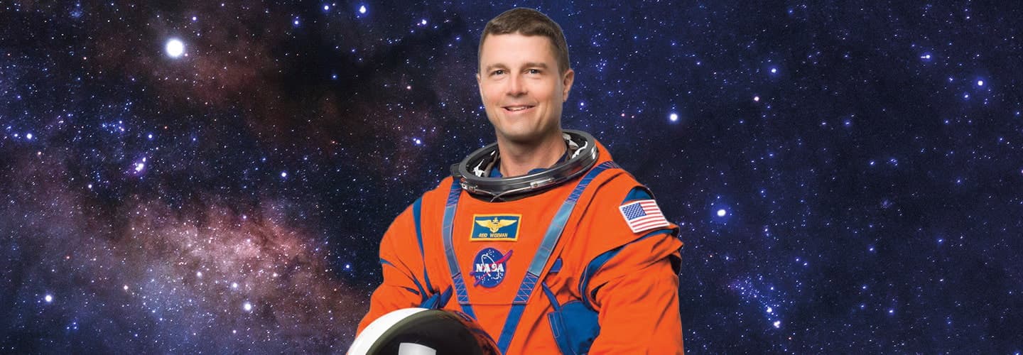 NASA astronaut Reid Wiseman holds a helmet against a starry background