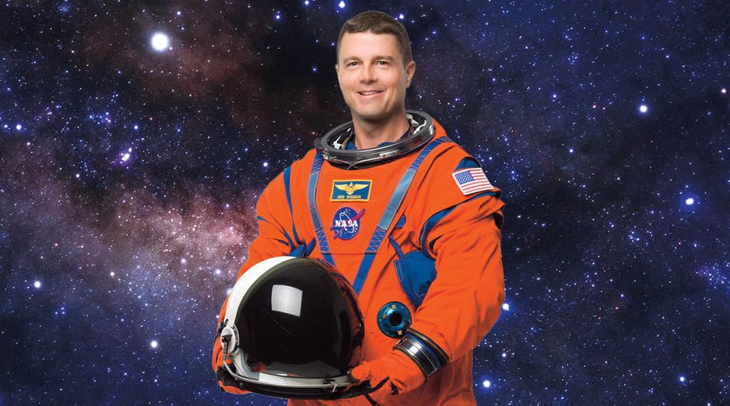 NASA astronaut Jed Wiseman holds a helmet and wears an orange flight suit