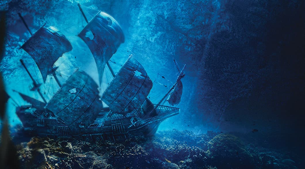 A sunken tall ship with tattered sails rests on the ocean floor in dim blue light