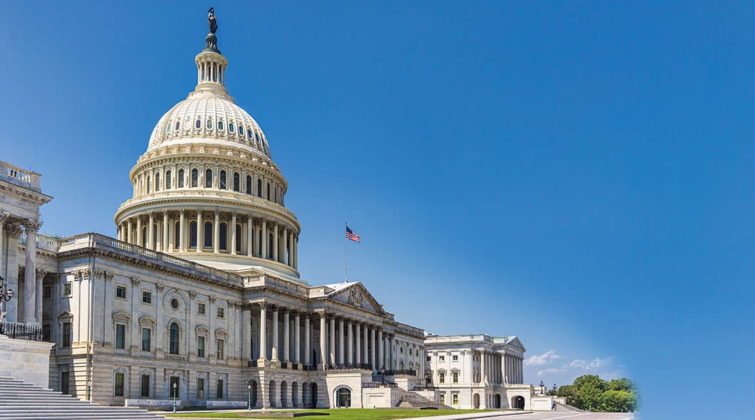 The United States Capitol building with its dome and an American flag against a clear sky